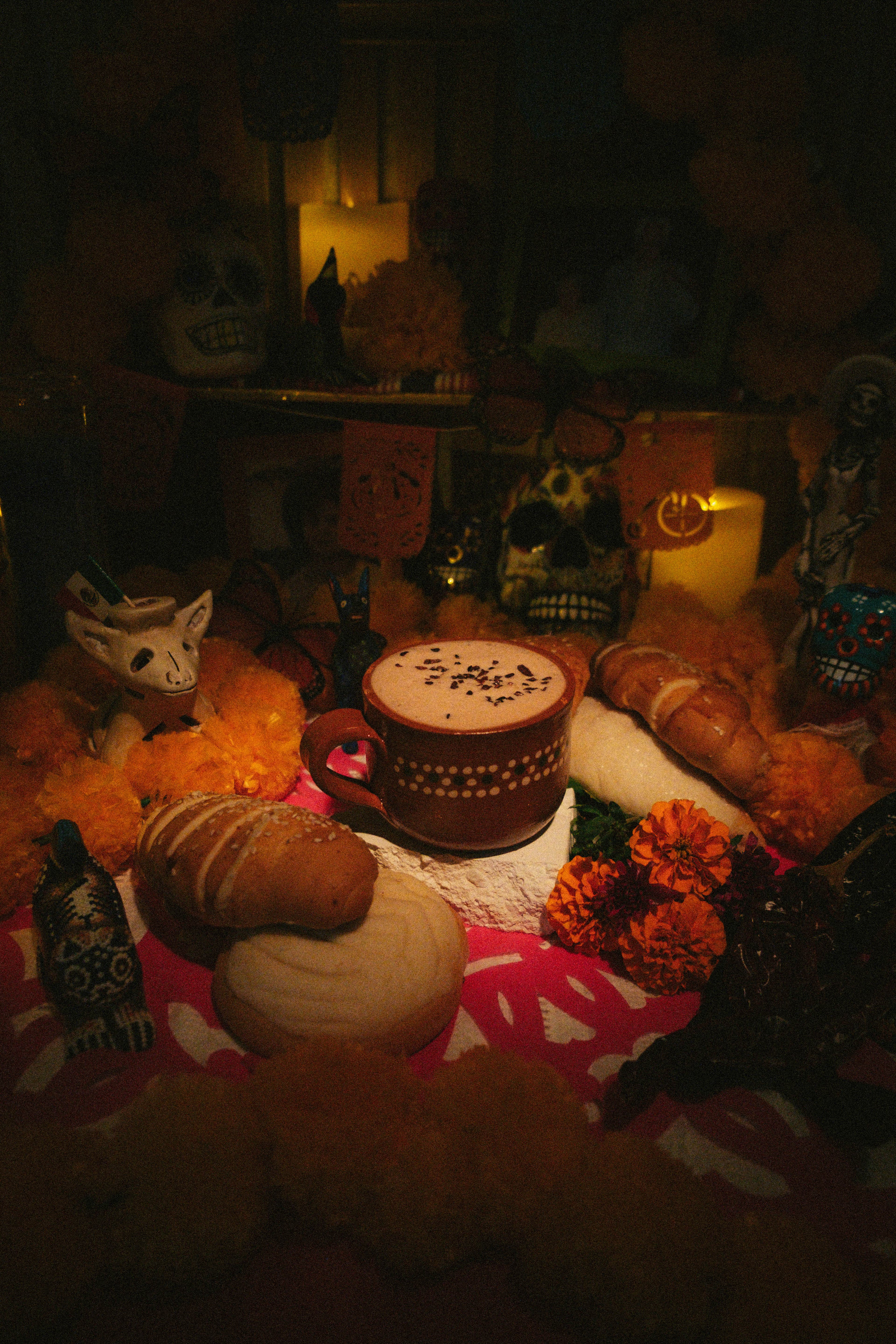Champurrado espumoso en una taza de barro sobre la ofrenda, junto a pan dulce y cempasúchil