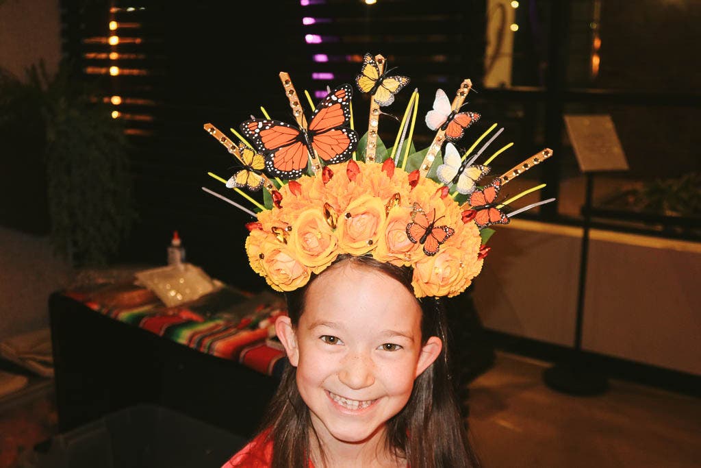 Una pequeña invitada con una corona de flores de Catrina de rosas naranjas y mariposas monarca